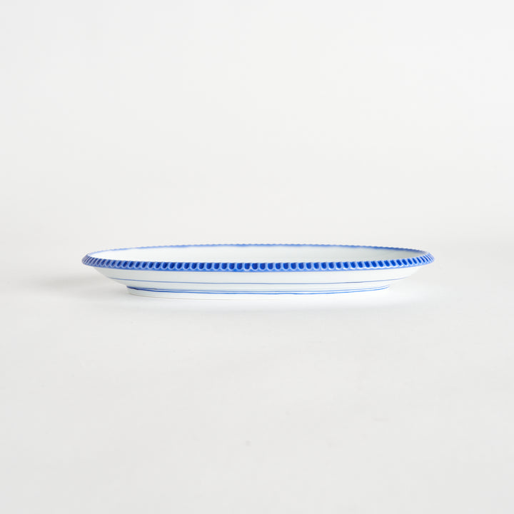 Side view of an oval salad plate showcasing its delicate shape and scalloped blue edge.