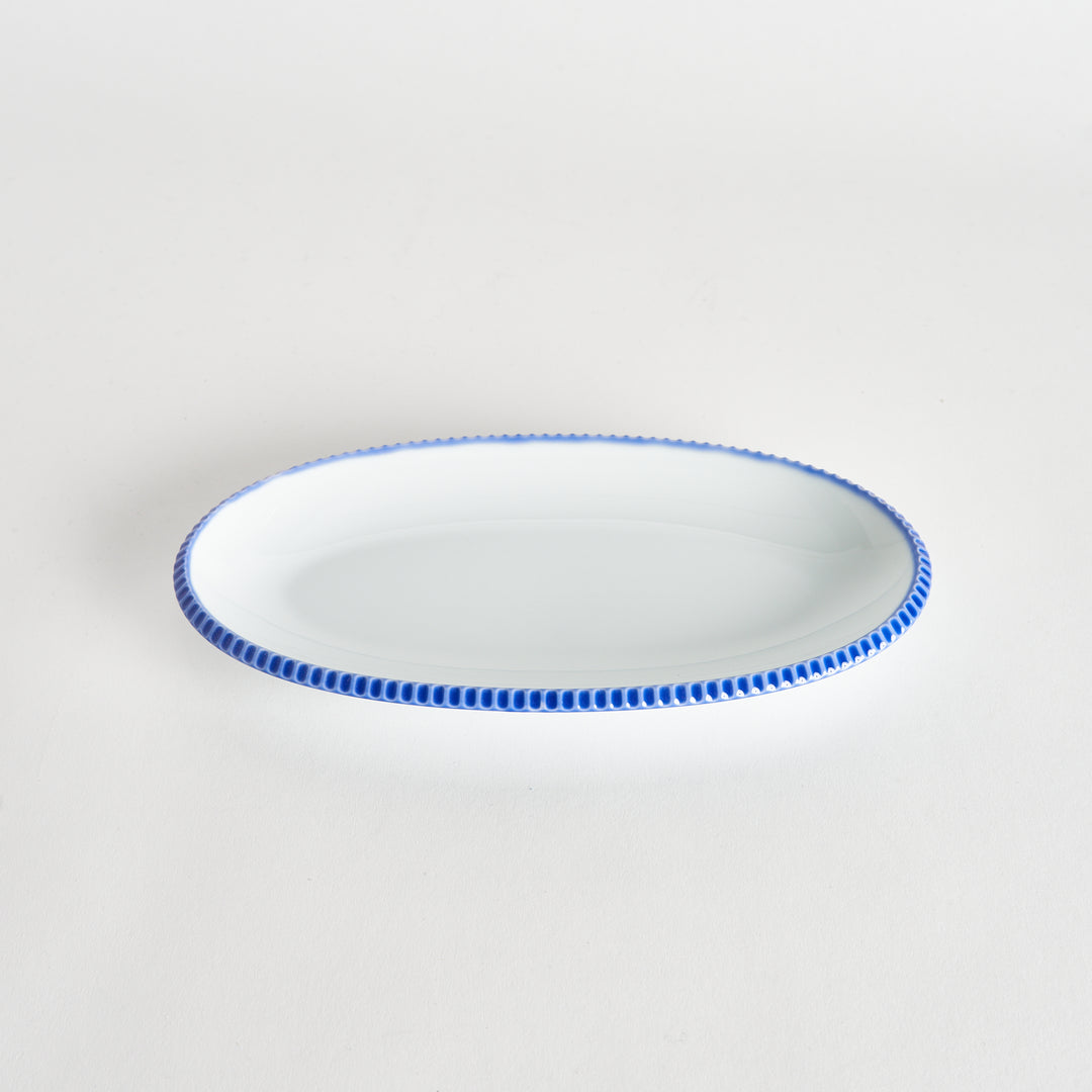 Angled view of an oval salad plate featuring a scalloped blue edge.