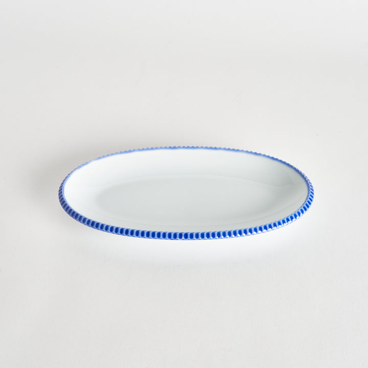 Angled view of an oval salad plate featuring a scalloped blue edge.