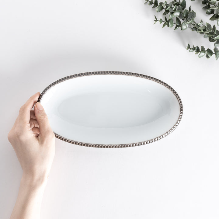 Handheld top-down view of an oval salad plate with an olive-colored scalloped edge.