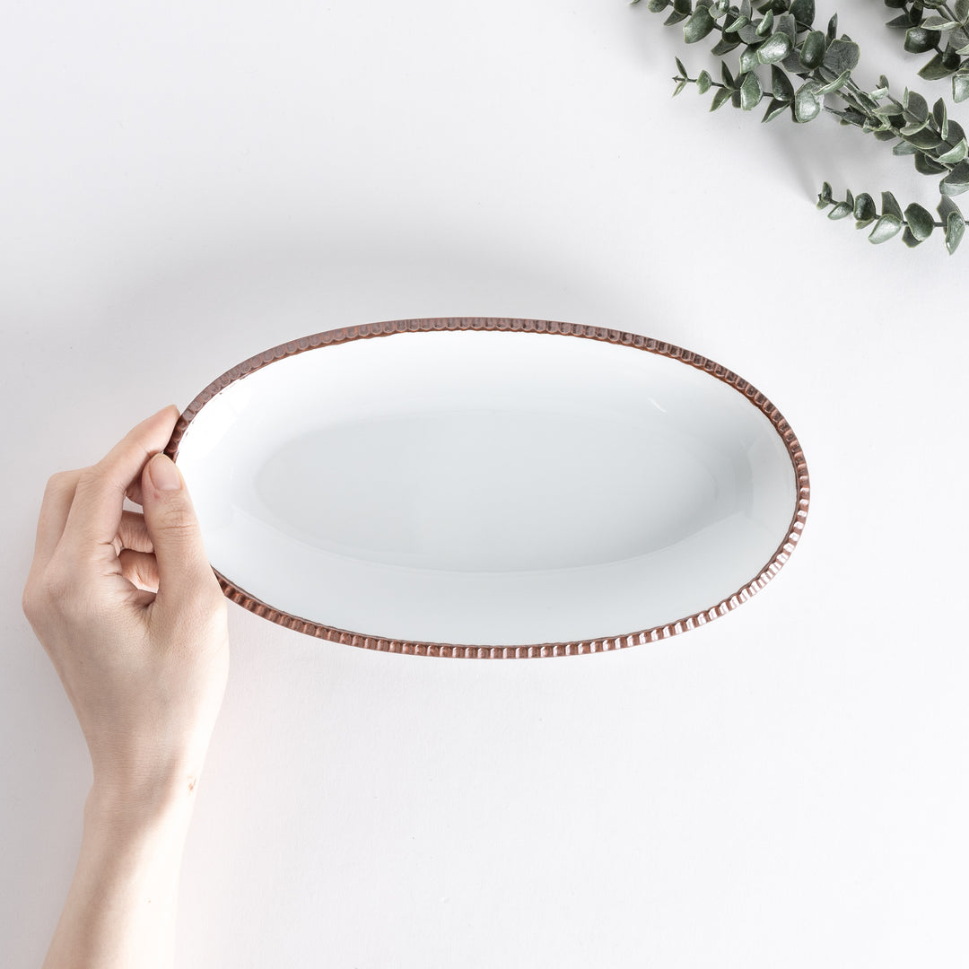 Handheld top-down view of an oval salad plate with a brown-colored scalloped edge.