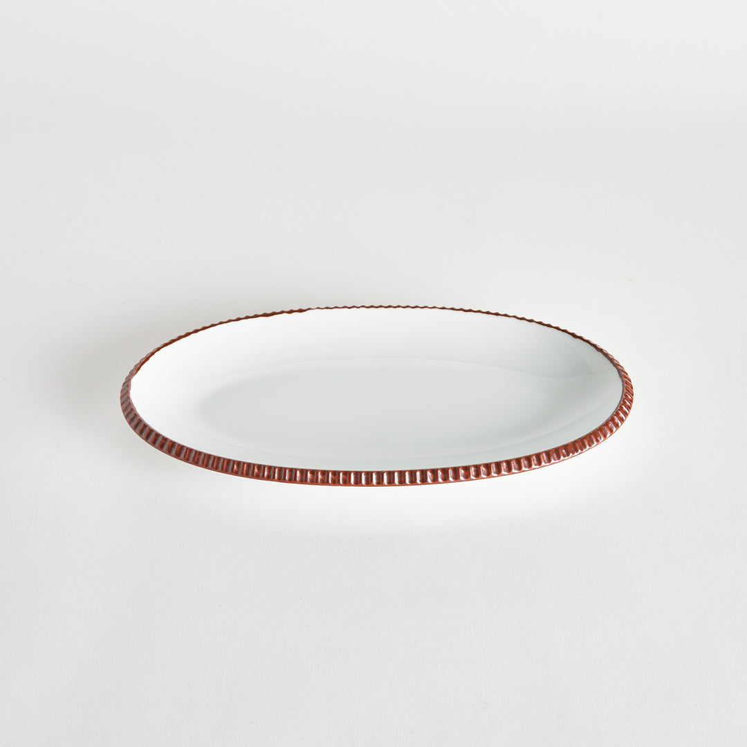 Angled view of an oval salad plate with a brown-colored scalloped edge.