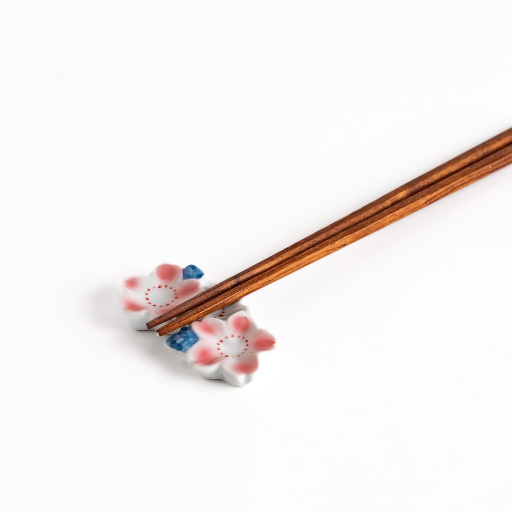 Sakura Blossom Chopstick Rest holding wooden chopsticks, showcasing its intricate floral design and functional charm.