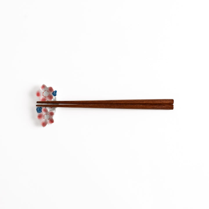 Sakura Blossom Chopstick Rest holding wooden chopsticks, showcasing its intricate floral design and functional charm.