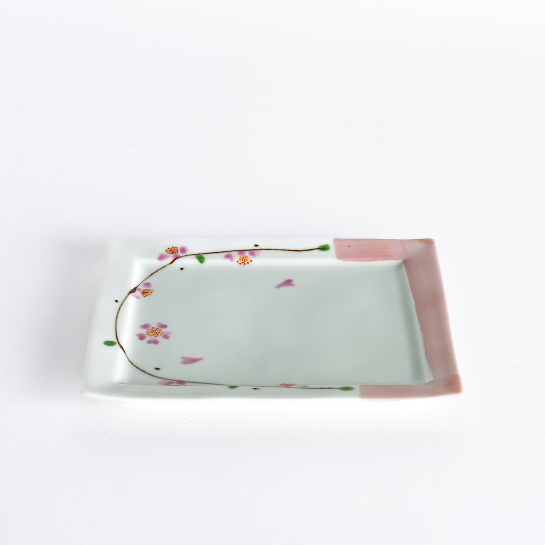 Dessert plate viewed at an angle, showing the pink cherry blossoms and delicate green accents along the edges.