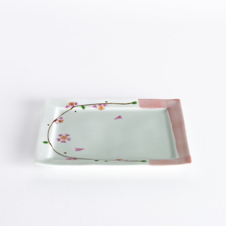 Dessert plate viewed at an angle, showing the pink cherry blossoms and delicate green accents along the edges.