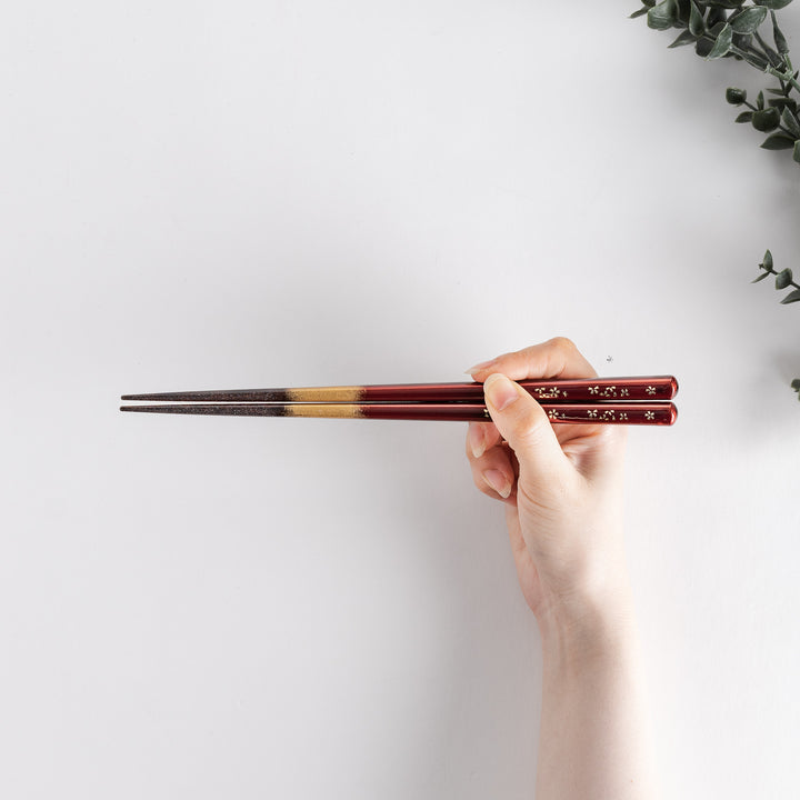 Elegant red and brown lacquered chopsticks adorned with delicate gold cherry blossom motifs, featuring a gradient of gold for added sophistication.