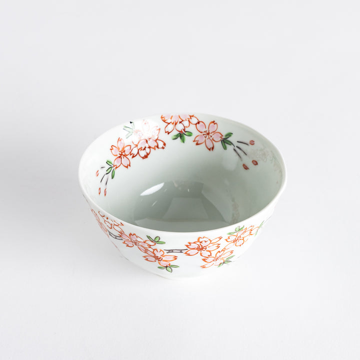 A white rice bowl adorned with delicate pink sakura blossoms and green leaves.