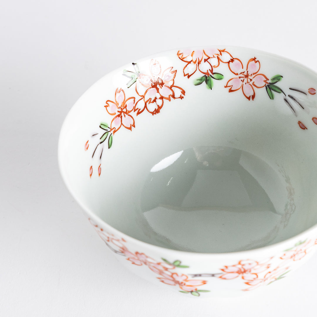 A white rice bowl adorned with delicate pink sakura blossoms and green leaves.