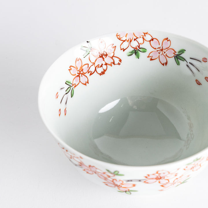 A white rice bowl adorned with delicate pink sakura blossoms and green leaves.