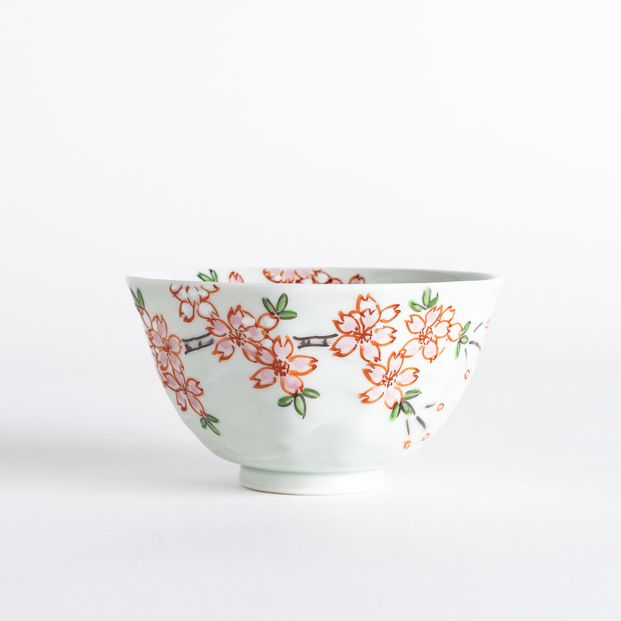 A white rice bowl adorned with delicate pink sakura blossoms and green leaves.