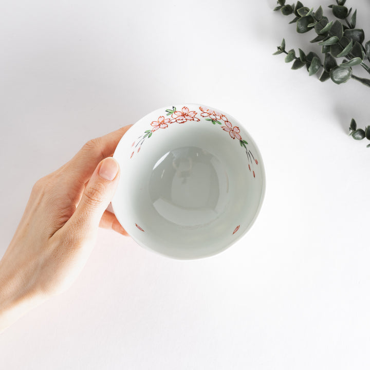 A white rice bowl adorned with delicate pink sakura blossoms and green leaves.