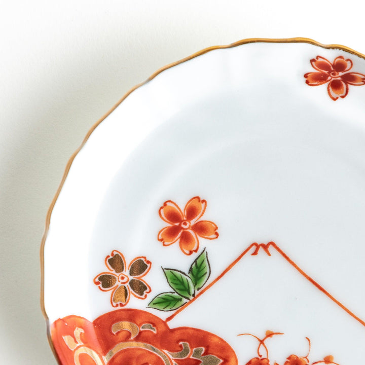 A white ceramic plate adorned with a red floral design and an outline of Mount Fuji in the background.