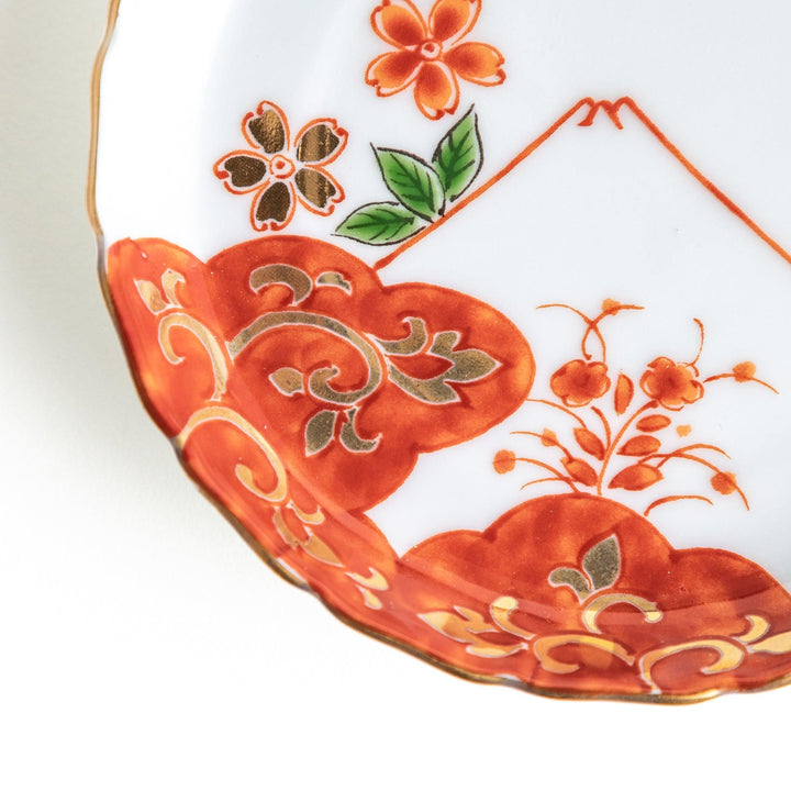 A white ceramic plate adorned with a red floral design and an outline of Mount Fuji in the background.