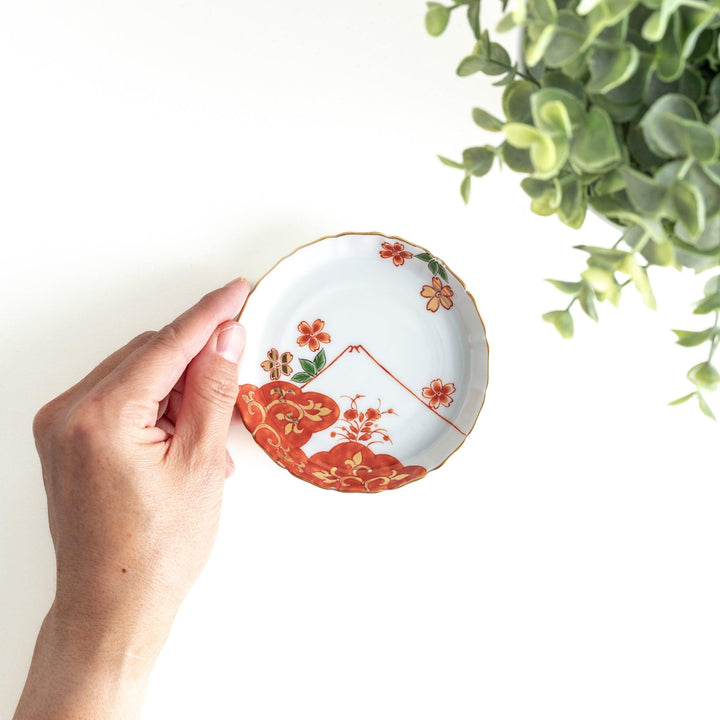 A white ceramic plate adorned with a red floral design and an outline of Mount Fuji in the background.