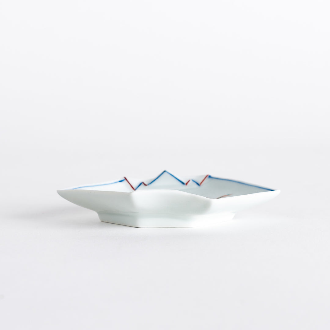 Low-angle view of a decorative sauce dish displaying its detailed landscape artwork and elegant shape.