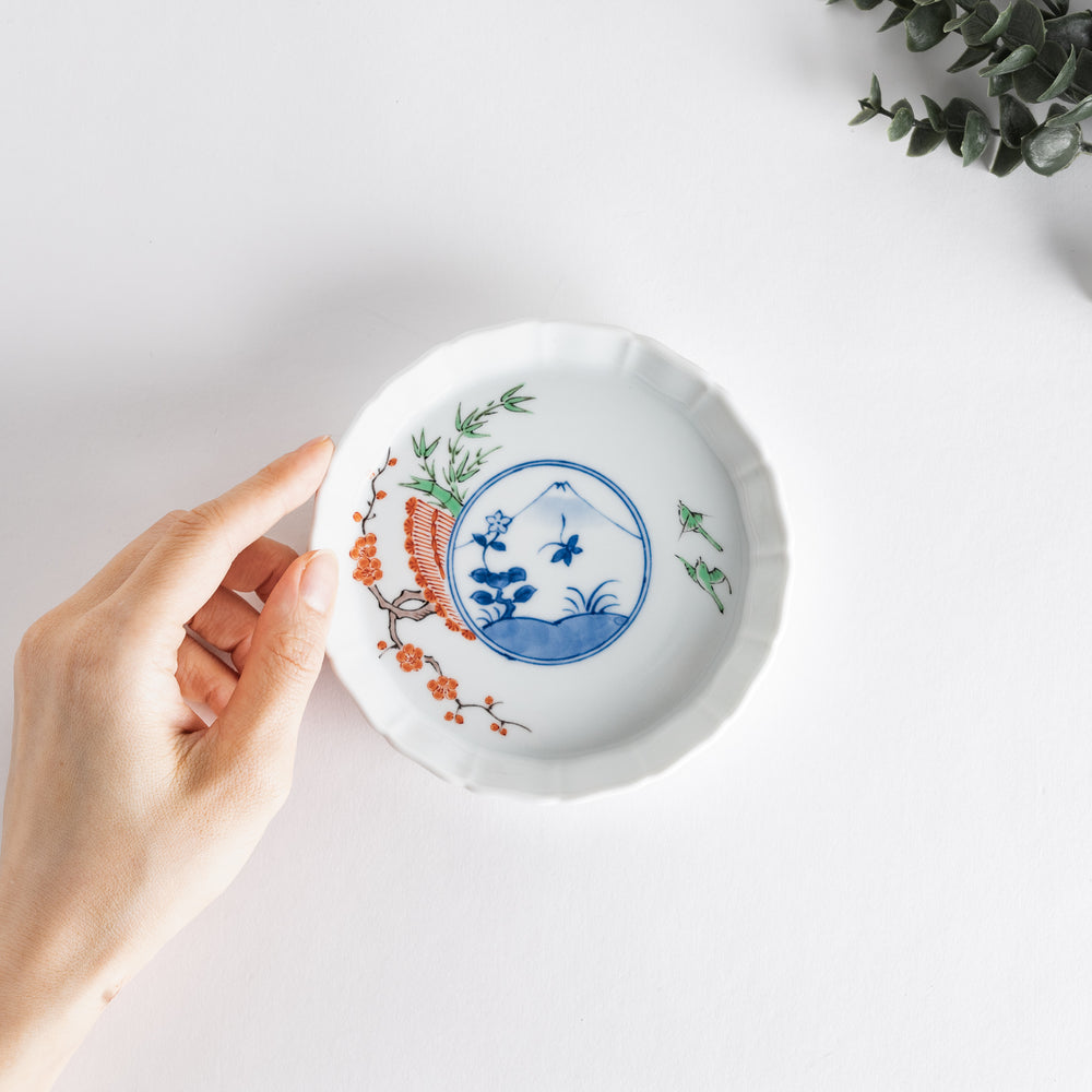 A small round plate with a traditional Japanese design depicting a landscape and floral elements.