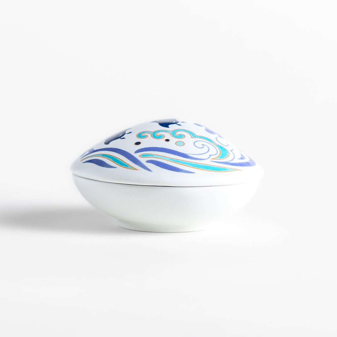 White ceramic incense holder shaped like a seashell, featuring an elegant blue wave and seabird motif, with a small rounded holder inside for secure incense placement.