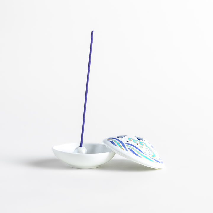 White ceramic incense holder shaped like a seashell, featuring an elegant blue wave and seabird motif, with a small rounded holder inside for secure incense placement.