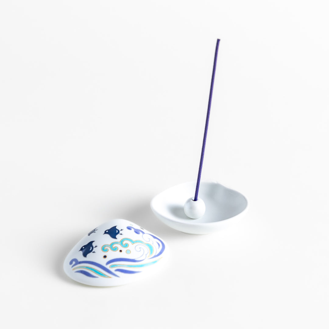 White ceramic incense holder shaped like a seashell, featuring an elegant blue wave and seabird motif, with a small rounded holder inside for secure incense placement.