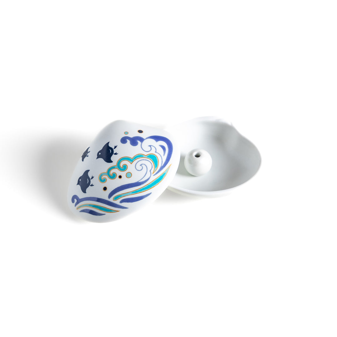 White ceramic incense holder shaped like a seashell, featuring an elegant blue wave and seabird motif, with a small rounded holder inside for secure incense placement.