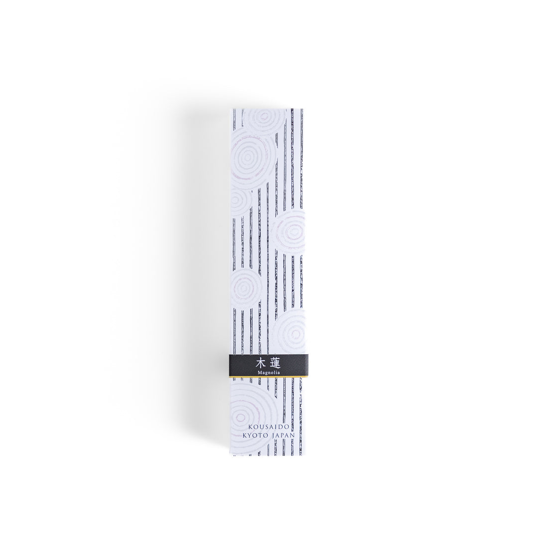 Incense in a light wooden box with deep brown sticks, elegantly packaged in a white design with subtle circular patterns and black accents, evoking a refined magnolia scent.