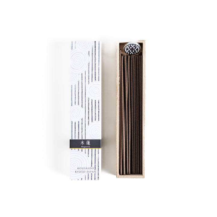 Incense in a light wooden box with deep brown sticks, elegantly packaged in a white design with subtle circular patterns and black accents, evoking a refined magnolia scent.