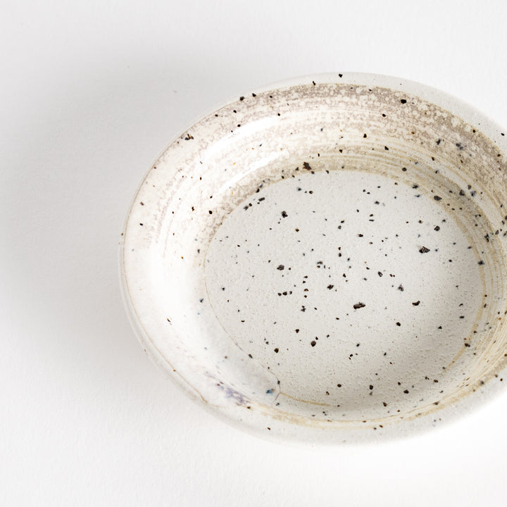 A shallow, off-white dish with a speckled glaze and a slightly textured finish.