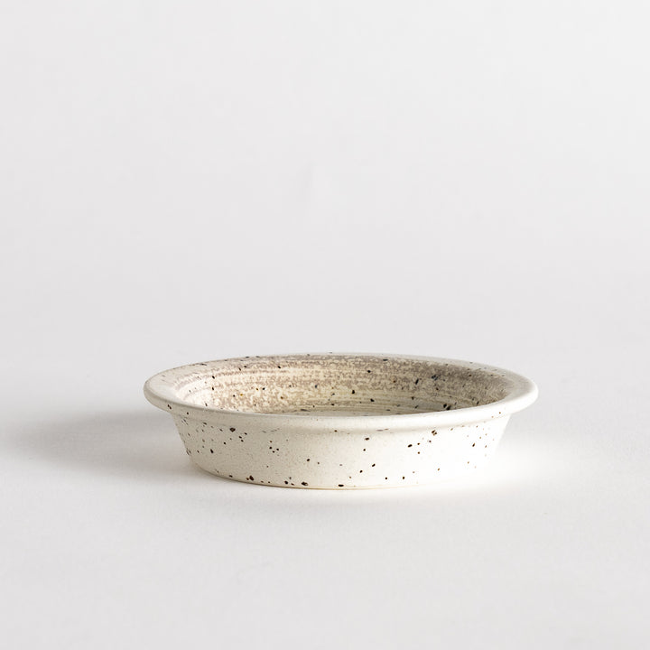 A shallow, off-white dish with a speckled glaze and a slightly textured finish.