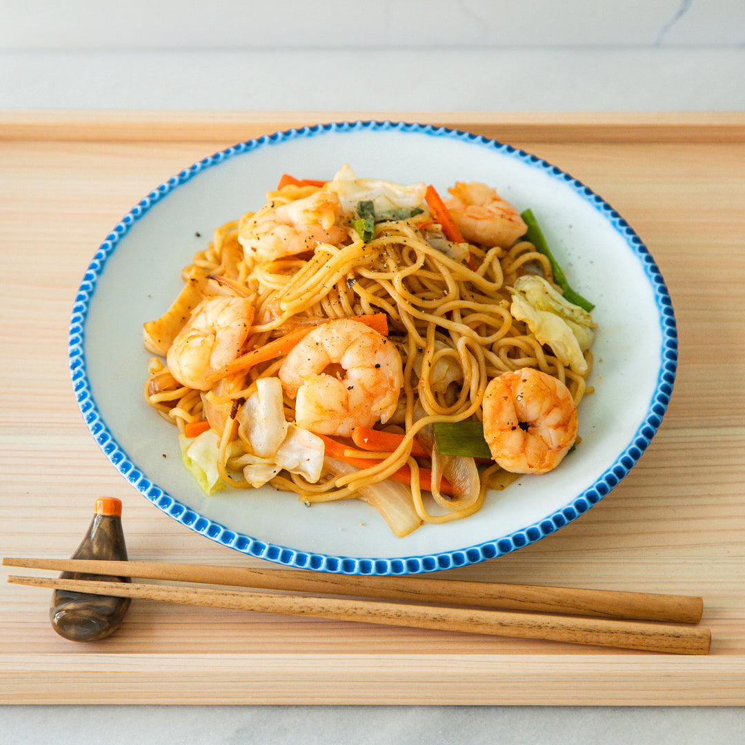 Top view of a plate of shrimp yakisoba with stir-fried noodles, vegetables, and shrimp, served with chopsticks.