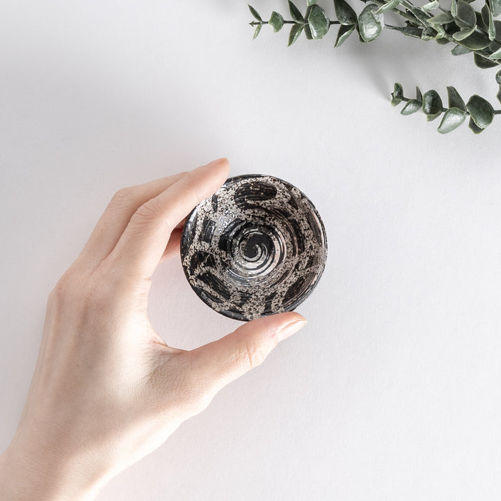 Overhead view of the silver rustic finish sake cup, held by hand, showing its spiral design and silver accents inside.