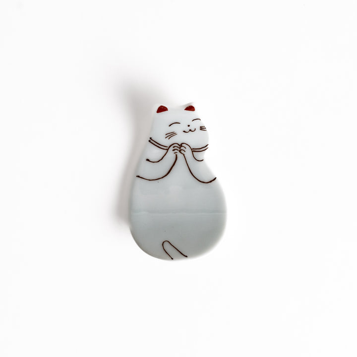 Ceramic chopsticks rest shaped like a sleeping cat, featuring delicate line art in brown and red accents, with a glossy white glaze finish.