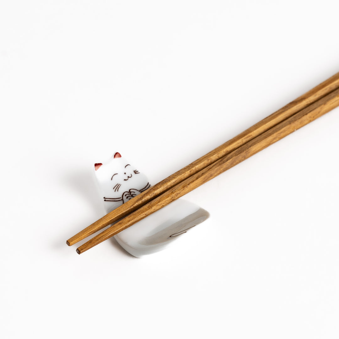 Ceramic sleeping cat-shaped chopsticks rest with chopsticks placed, showcasing its elegant brown and red line art details.