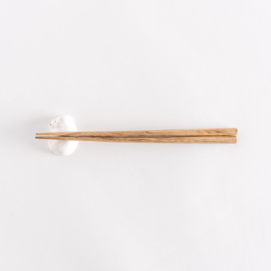 Slightly angled view of a chopstick rest in the shape of a sleeping bear, with chopsticks placed on it.
