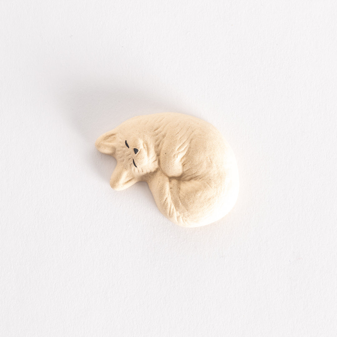 Chopstick rest shaped like a sleeping cat, with chopsticks placed on it, set against a white background.