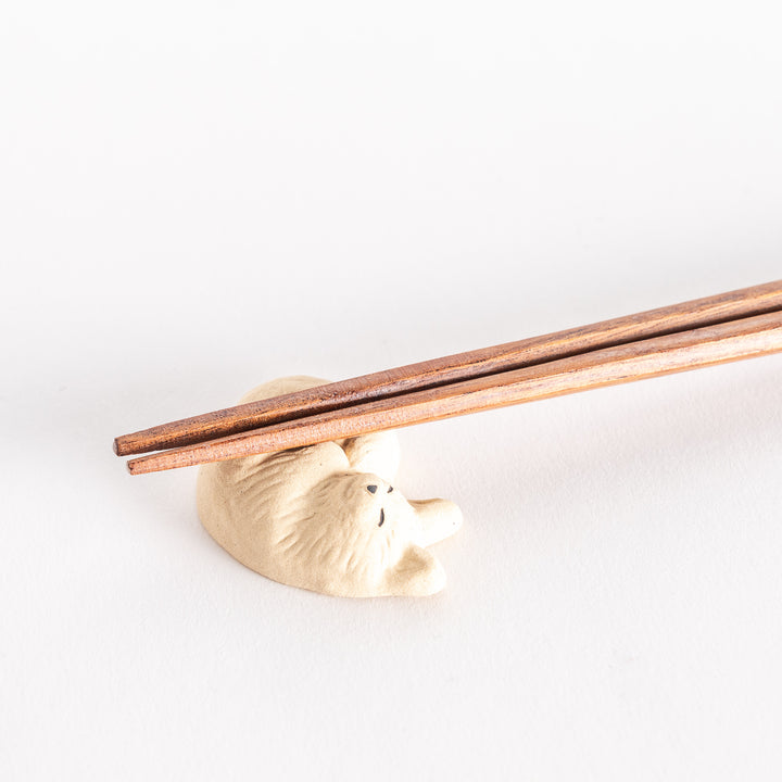 Close-up view of a chopstick rest in the shape of a sleeping cat, with chopsticks resting on it, focusing on the details of the cat’s form.