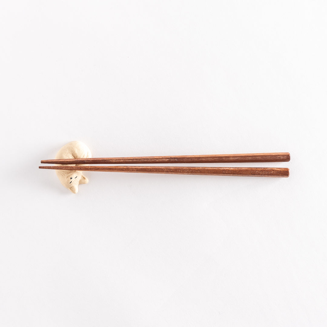 Slightly angled view of a chopstick rest in the shape of a sleeping cat, with chopsticks placed on it, highlighting the features of the cat.
