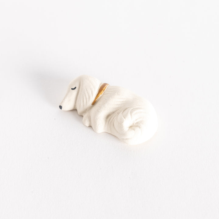 Angled view of a white ceramic sleeping dog chopstick rest, highlighting its soft curves and gold collar.