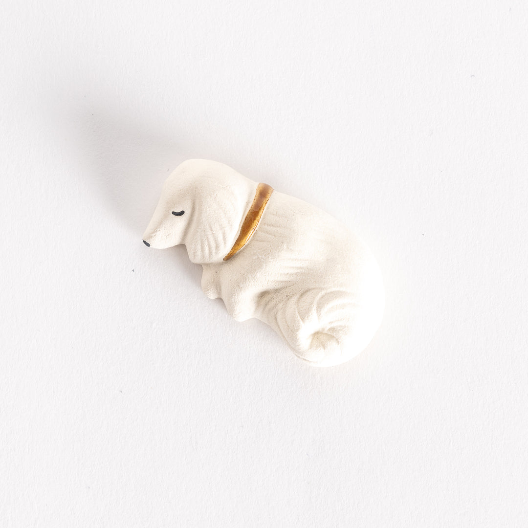 A white ceramic chopstick rest shaped like a sleeping dog, featuring a gold collar.