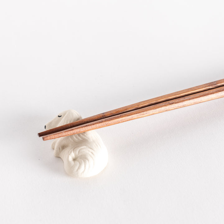 Close-up of a white ceramic sleeping dog chopstick rest with chopsticks resting on its back.