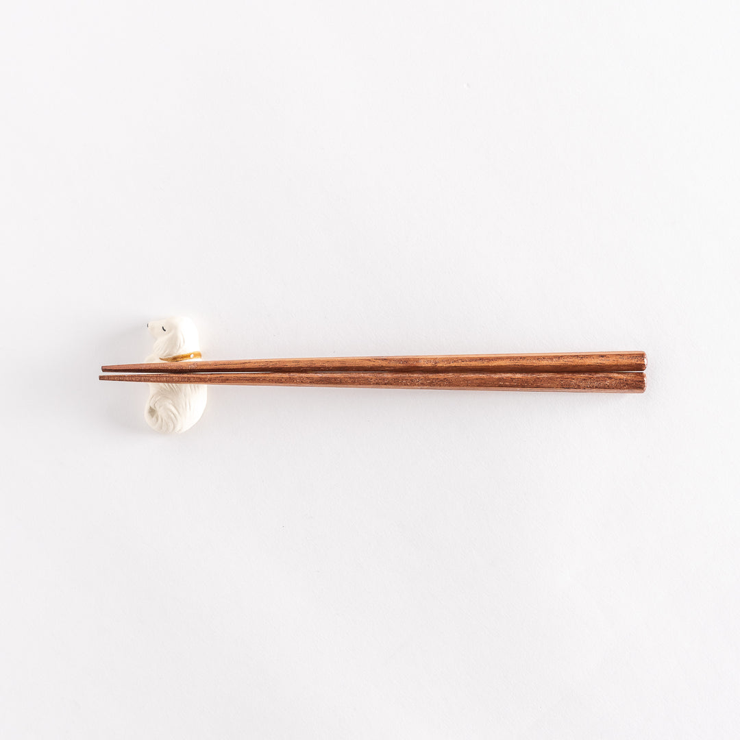 Wide shot of a white ceramic sleeping dog chopstick rest holding chopsticks across its back.