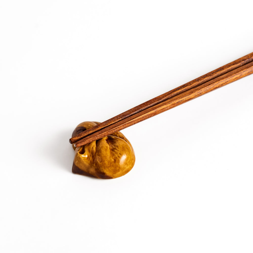 Wooden chopsticks resting on a charming brown ceramic chopstick rest shaped like a sleeping squirrel.