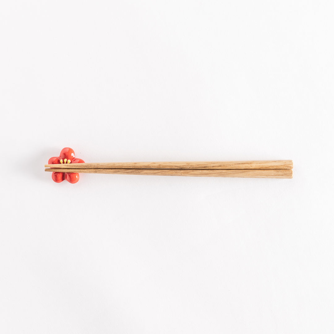 Red plum chopsticks rest with wooden chopsticks placed on it.