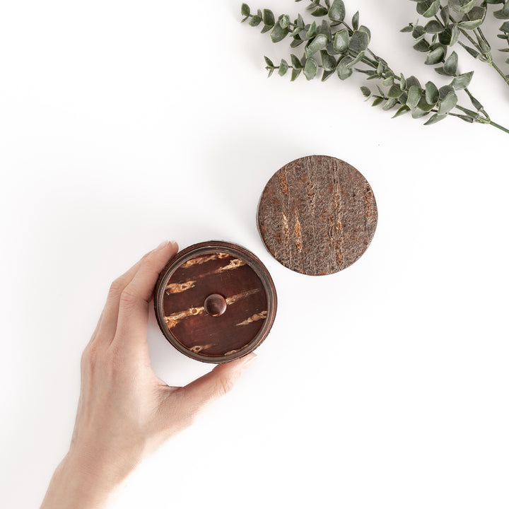 Hand holding a rustic cherry bark tea caddy with a separate lid, showcasing the natural beauty and texture of the bark, perfect for storing loose leaf tea.