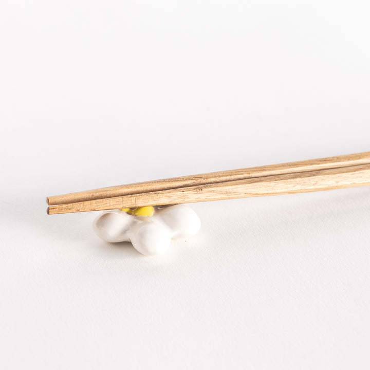 Close-up of a white plum chopsticks rest holding wooden chopsticks.