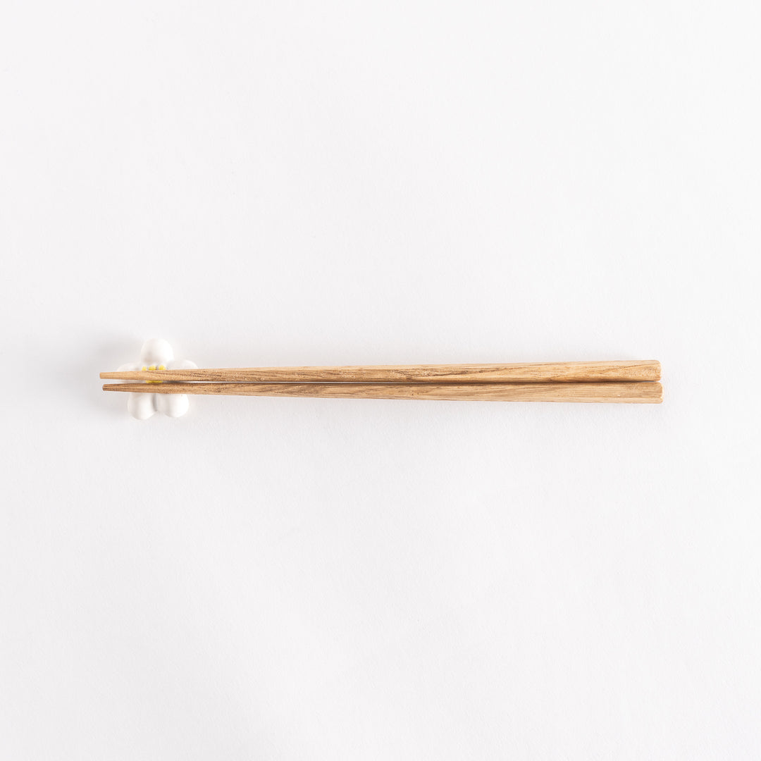 White plum chopsticks rest with wooden chopsticks placed on it.