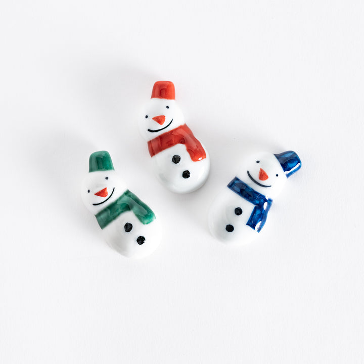 A set of three ceramic snowman chopstick rests, each wearing a colorful scarf and hat in green, red, and blue.