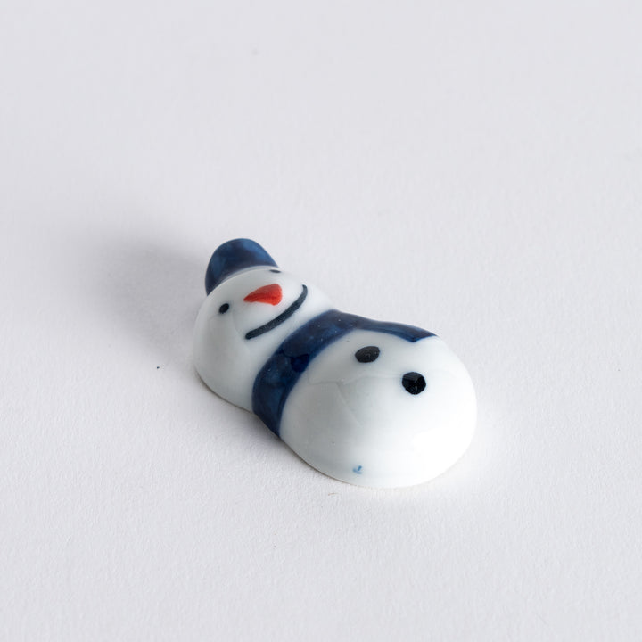 Diagonal angle view of snowman chopstick rest with a blue hat and scarf, emphasizing its fun and festive design.