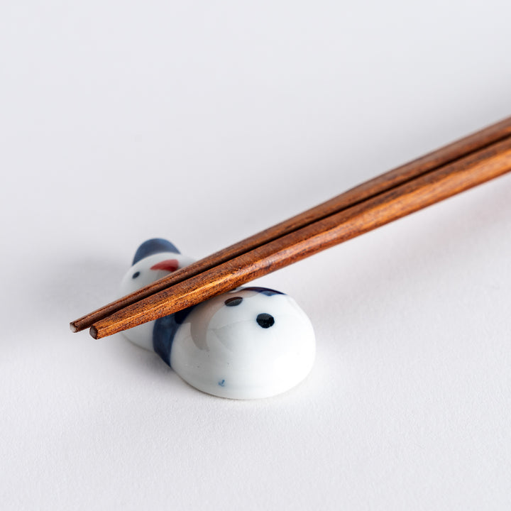 Close-up of snowman chopstick rest with chopsticks placed on it, highlighting the blue hat and scarf design.