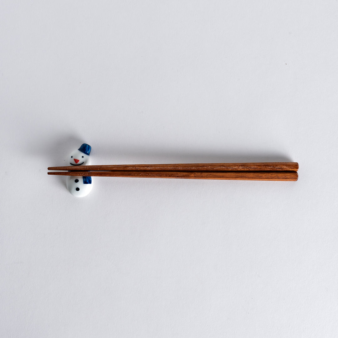 Full view of snowman chopstick rest with chopsticks resting on it, showcasing the playful snowman design with a blue hat and scarf.